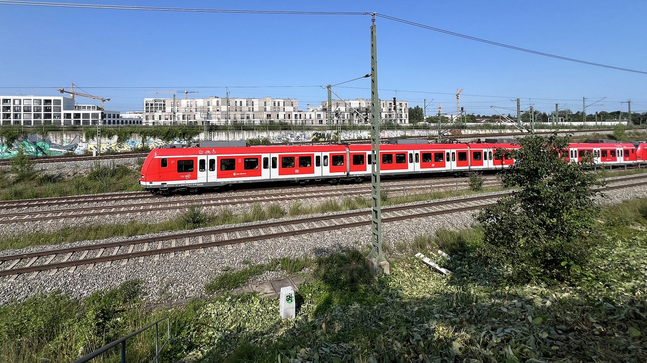 Eine S-Bahn fährt auf der Strecke Pasing-Obermenzing. Im Hintergrund sind Häuserblocks.