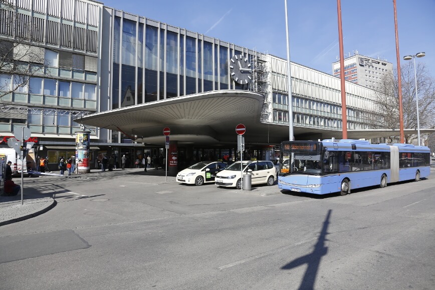 Das Empfangsgebäude des Münchner Hauptbahnhofs, vor dem Autos und ein Bus stehen.