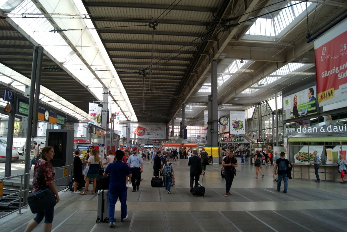Die Bahnhofshalle mit Läden und vielen Menschen und ein Teil des Hallendachs.