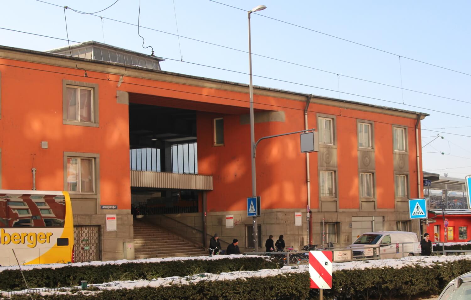 Das alte, orangene Empfangsgebäude des Starnberger Bahnhofs und davor parkende Autos.
