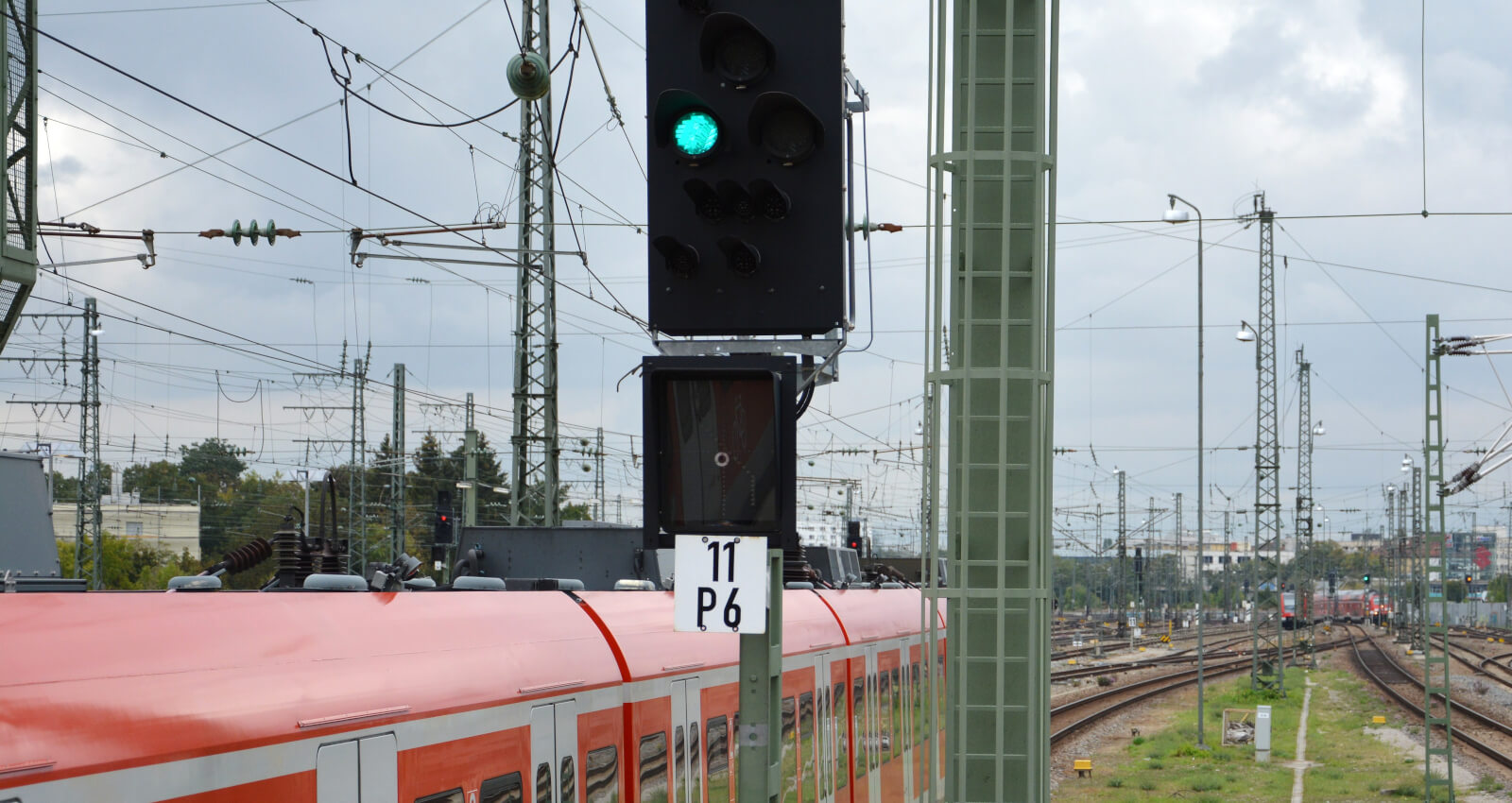 Auf einer Bahnstrecke fährt ein Regionalzug und im Vordergrund leuchtet eine Ampel grün