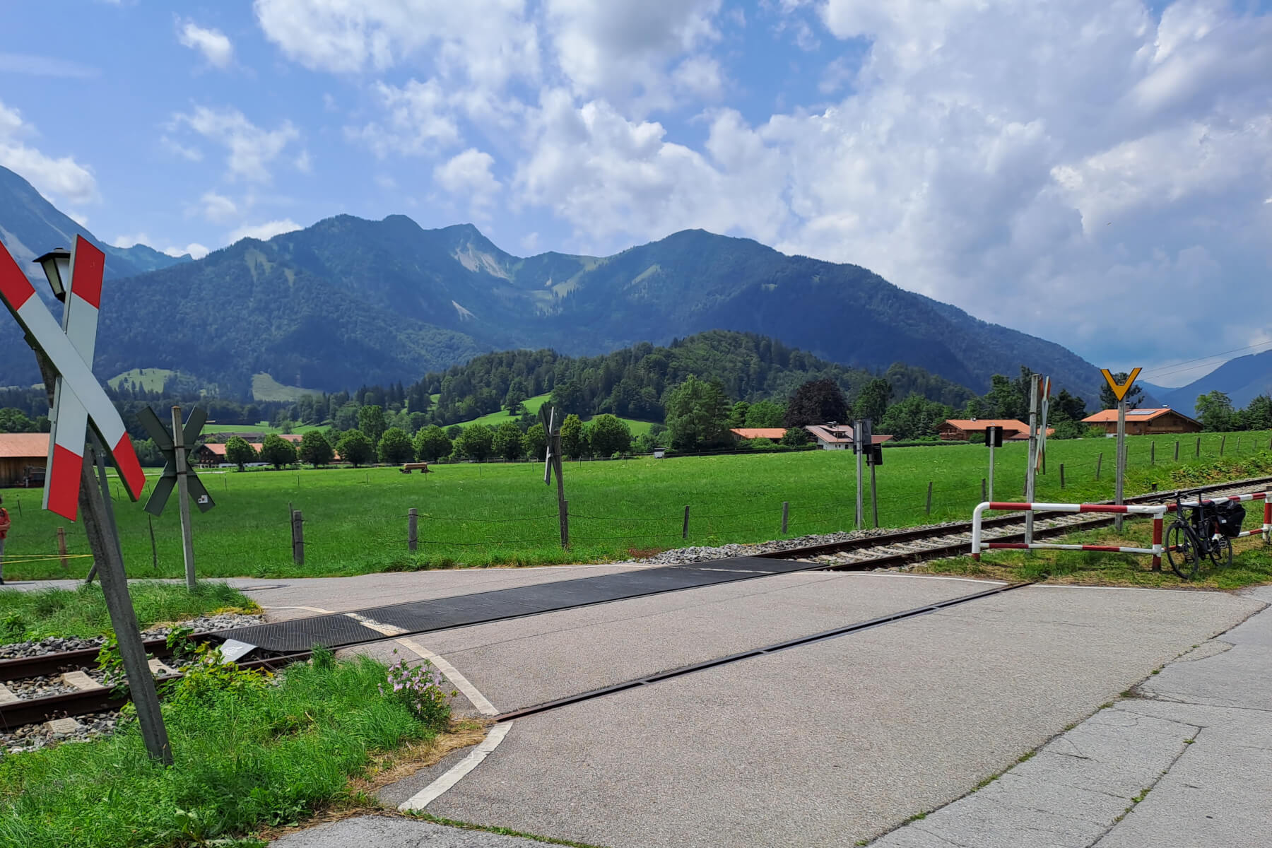 Der Bahnübergang in Osterhofen mit Grünflächen und Bergen im Hintergrund.