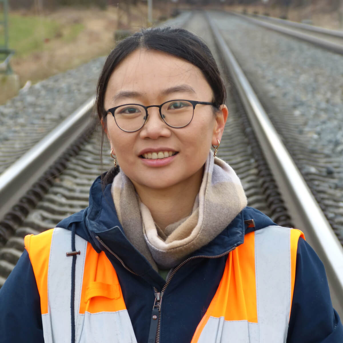 Lidan Jin in Sicherheitsweste steht auf Eisenbahngleisen