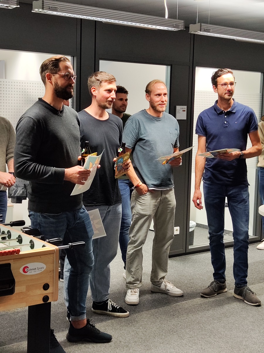 Vier Teilnehmende des Kicker-Turniers stehen in einer Reihe und halten eine Urkunde.