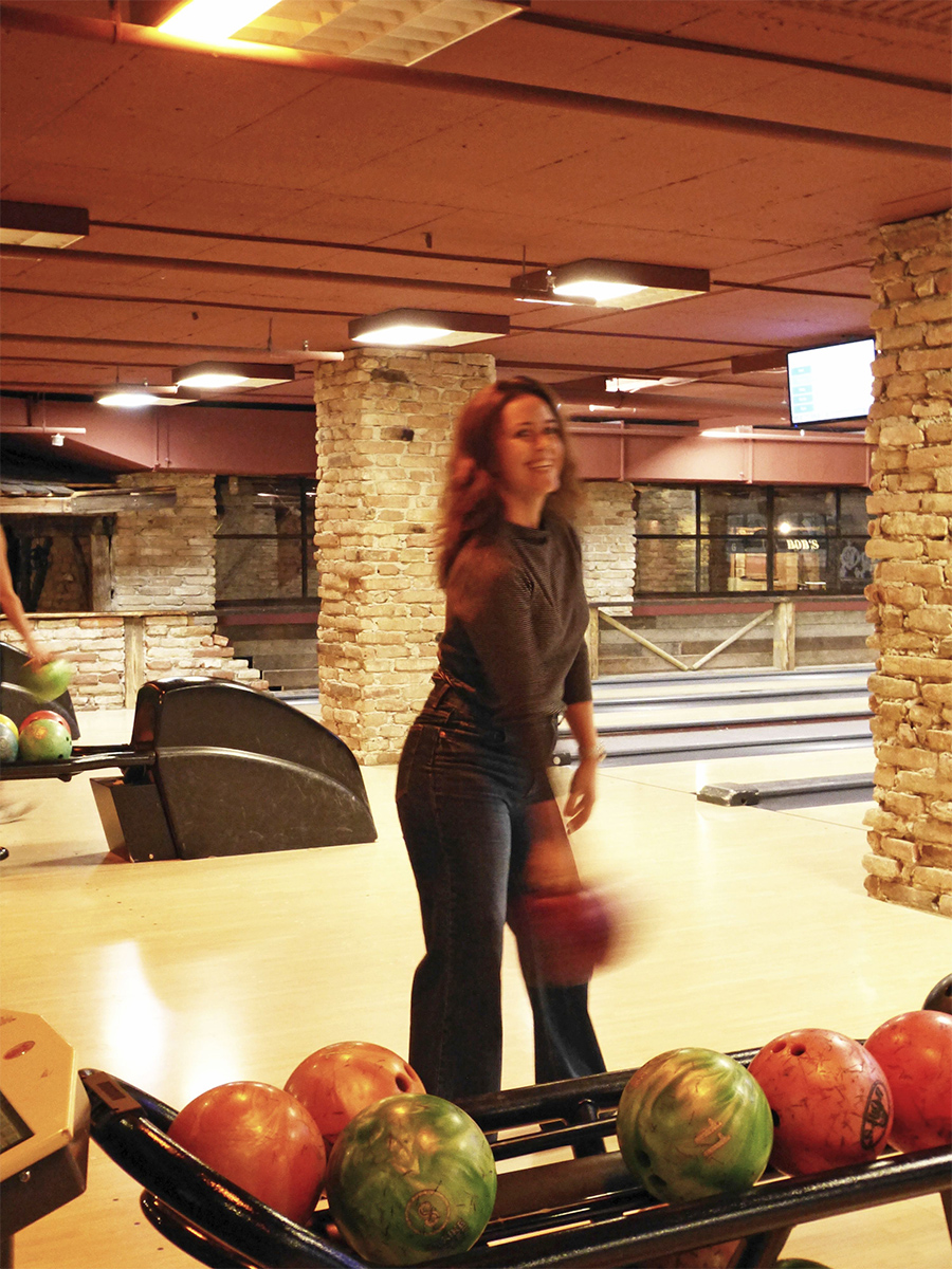 Eine Mitarbeitende mit einer Bowling-Kugel steht vor der Bowling-Bahn.