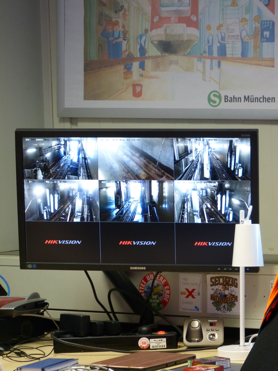 Ein Monitor steht auf einem Schreibtisch. Auf dem Monitor können in verschiedenen Abschnitten Video-Überwachungen verschiedener Bereiche überprüft werden.