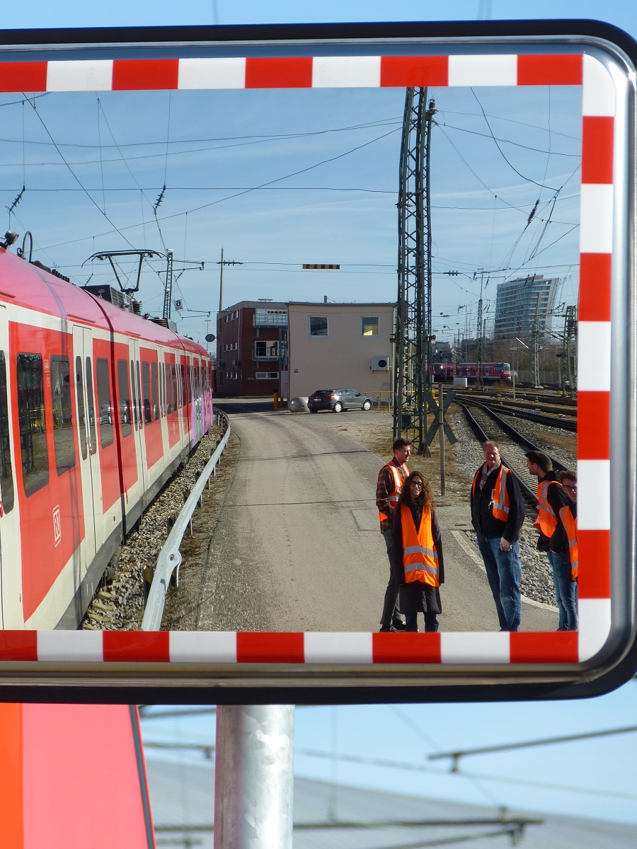 In einem Verkehrsspiegel sind mehrere Mitarbeitende in Schutzkleidung neben einer S-Bah stehend gespiegelt.