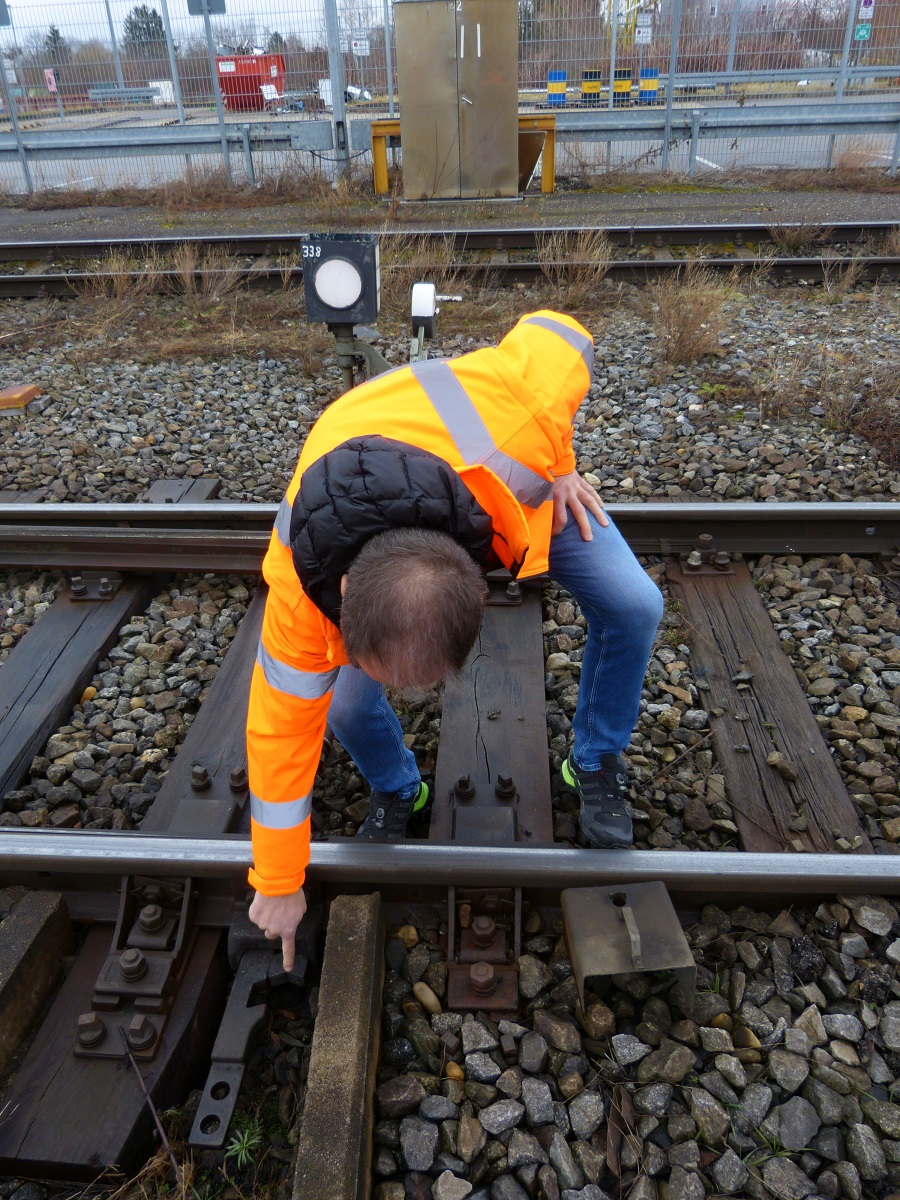 Ein Mann in Schutzkleidung zeigt auf die Weiche eines Gleises.