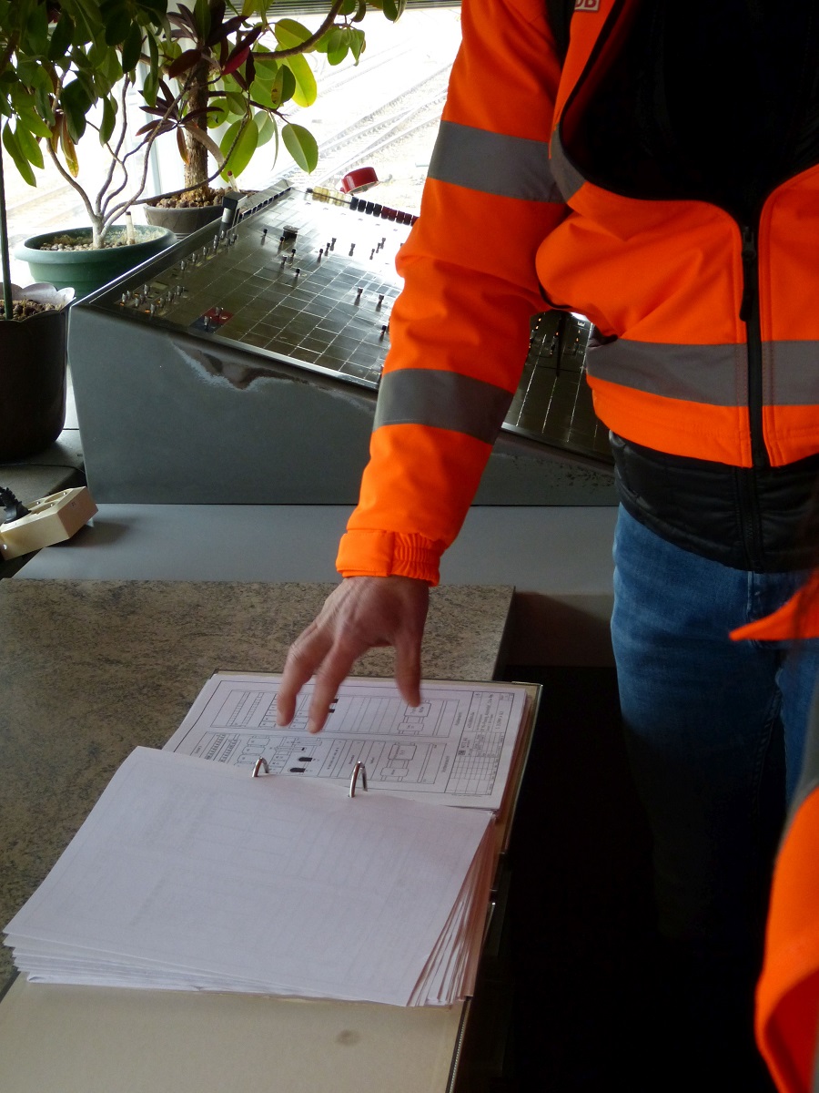 Ein Mensch in Schutzkleidung seigt auf ein in einem Order eingeheftetes Dokument.