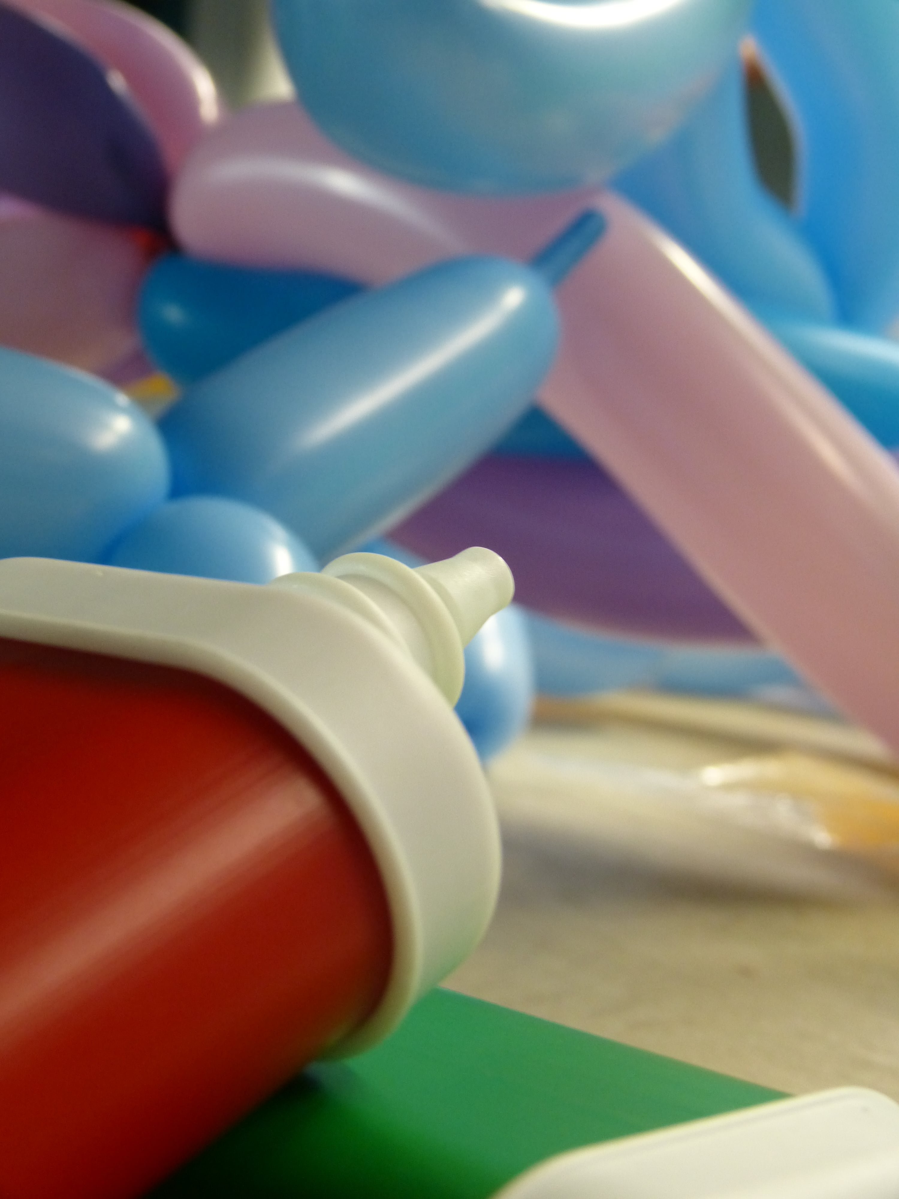 Nahaufnahme einer Luftpumpe für Ballons. Im Hintergrund liegen bereits aufgeblasene Ballons.