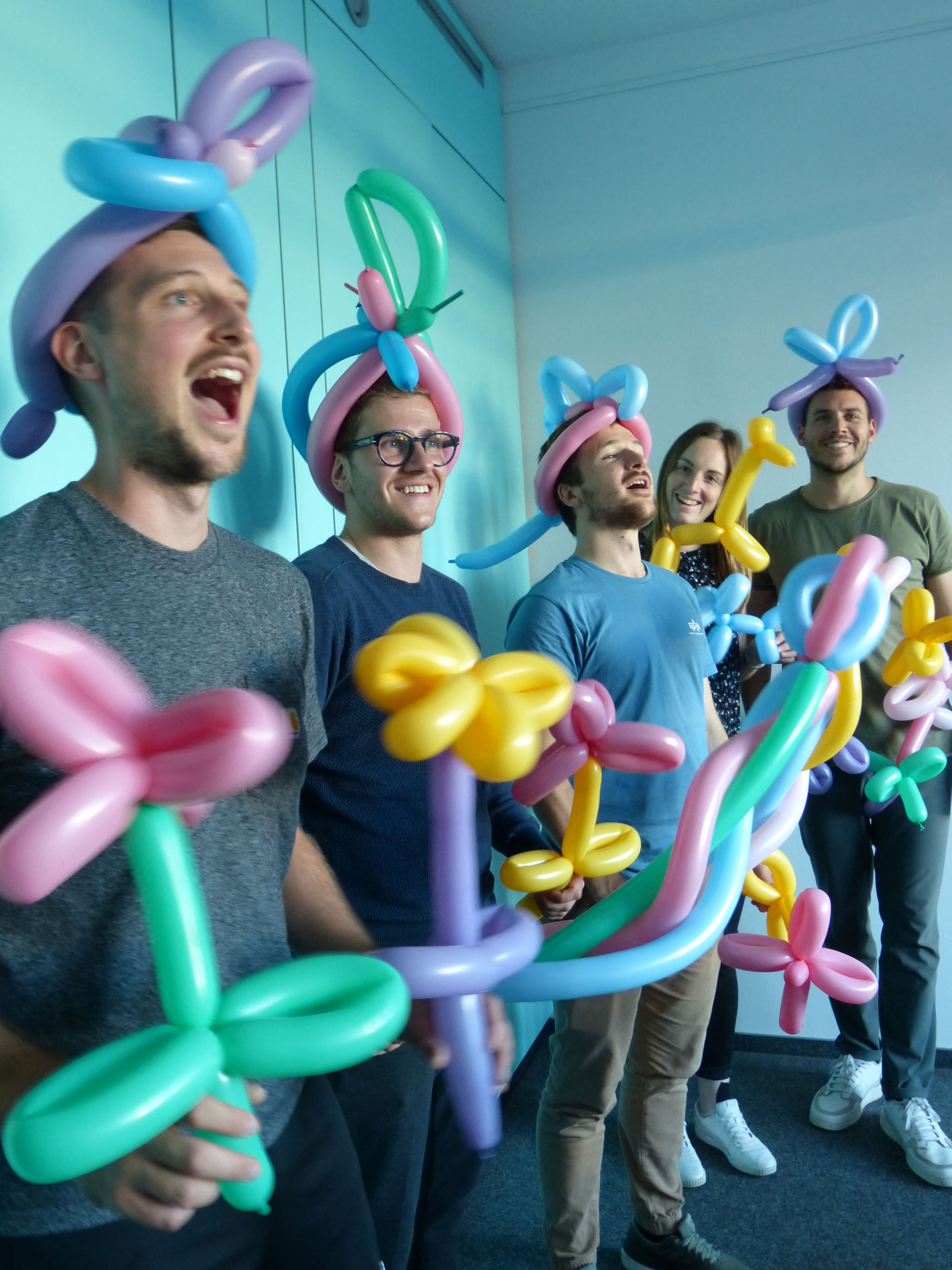 Mehrere Mitarbeitende haben Ballon-Tier-Hüte auf und Ballon-Blumen in der Hand.