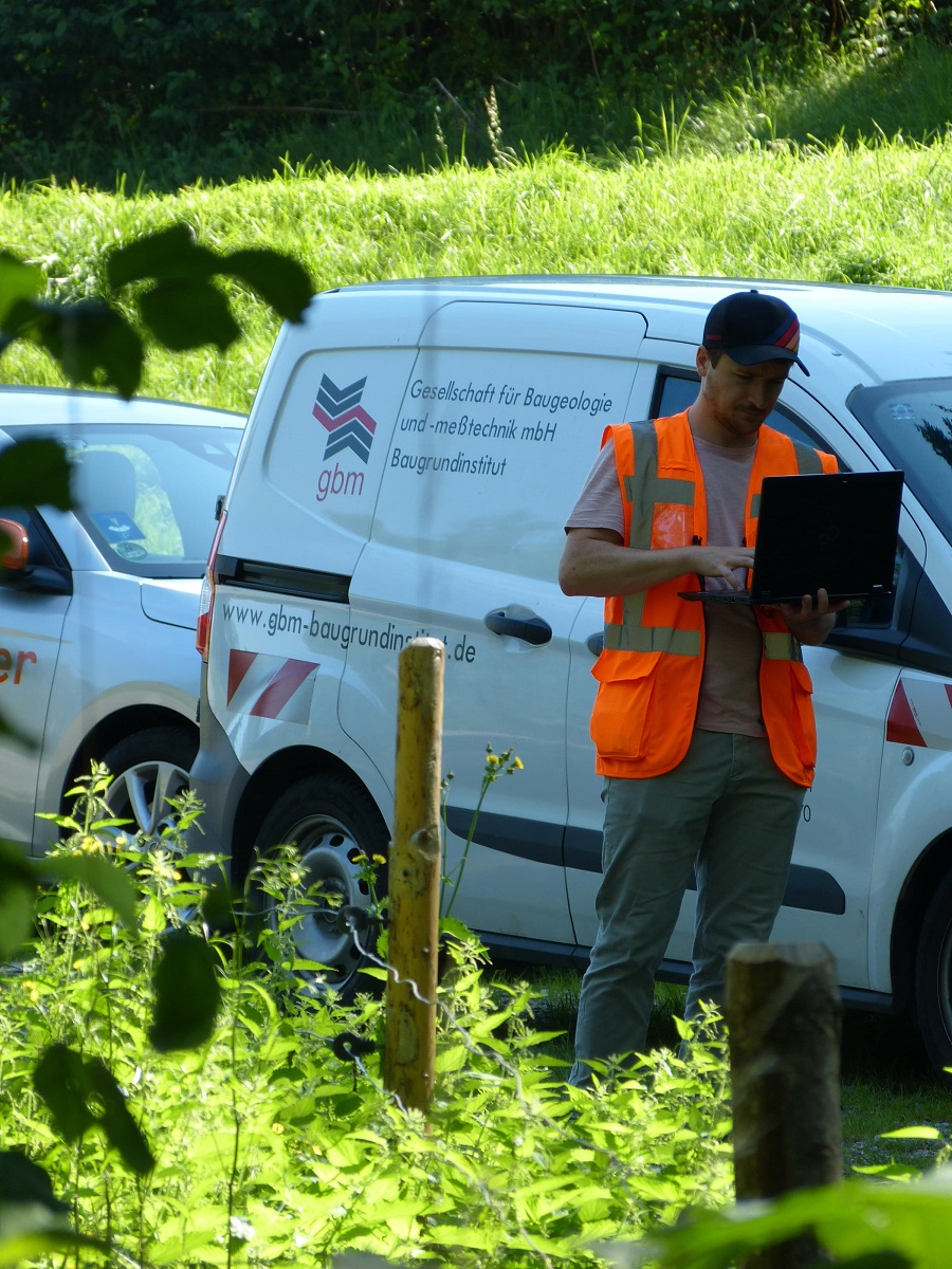 Ein DB-Ingenieur mit Laptop in der Hand vor einem Auto.