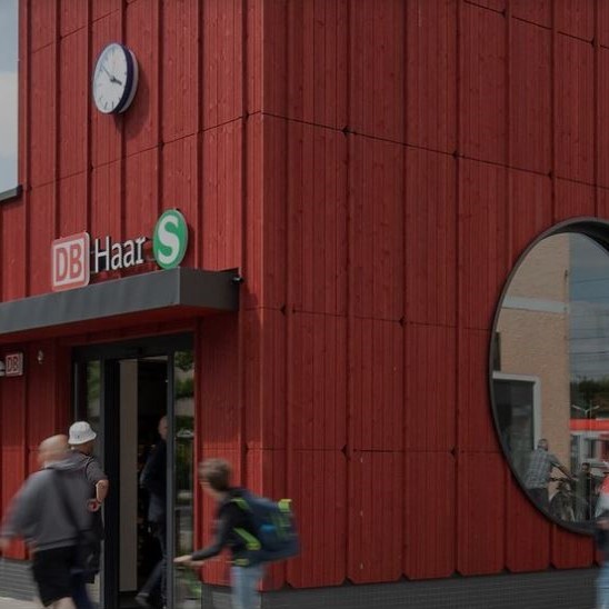 Der Eingang der S-Bahn Haltestelle Haar. Menschen gehen in das rote Gebäude.